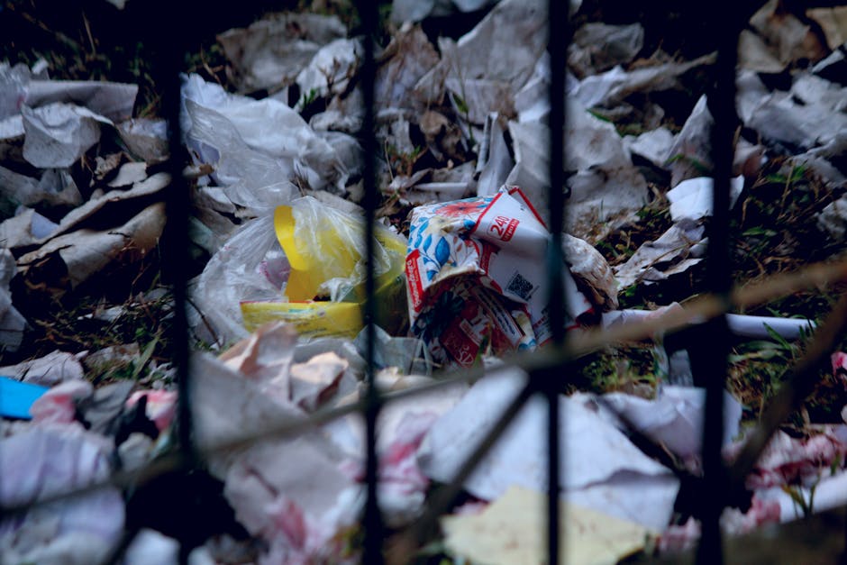 Indoor scene showing scattered cigarette butts on a dirty, textured surface, with some partially burnt and others intact, exhibiting various shades of brown, black, and white. The cigarette waste appears crumpled and crushed, mixed with ash deposits and small debris, creating a cluttered appearance. The background reveals a dimly lit environment with a rough, mottled floor surface, likely concrete or similar material. This image exemplifies waste that could be handled through alternative waste management methods such as on-site clearance or private disposal, which Rubbish Collection Merton provides as part of their rubbish removal services, especially for small-scale or informal rubbish accumulations.